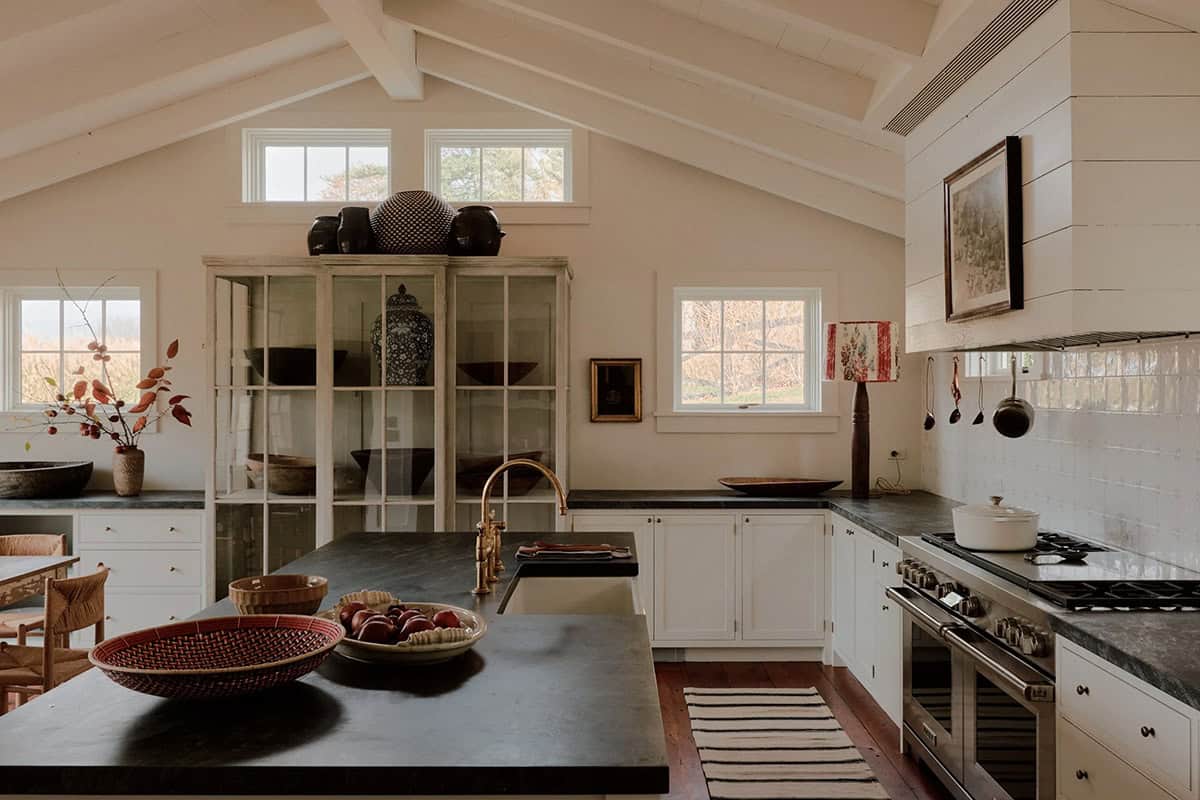Kitchen with white cabinets, soapstone countertops, brass faucet, vaulted ceiling, and glass-front pantry cabinet