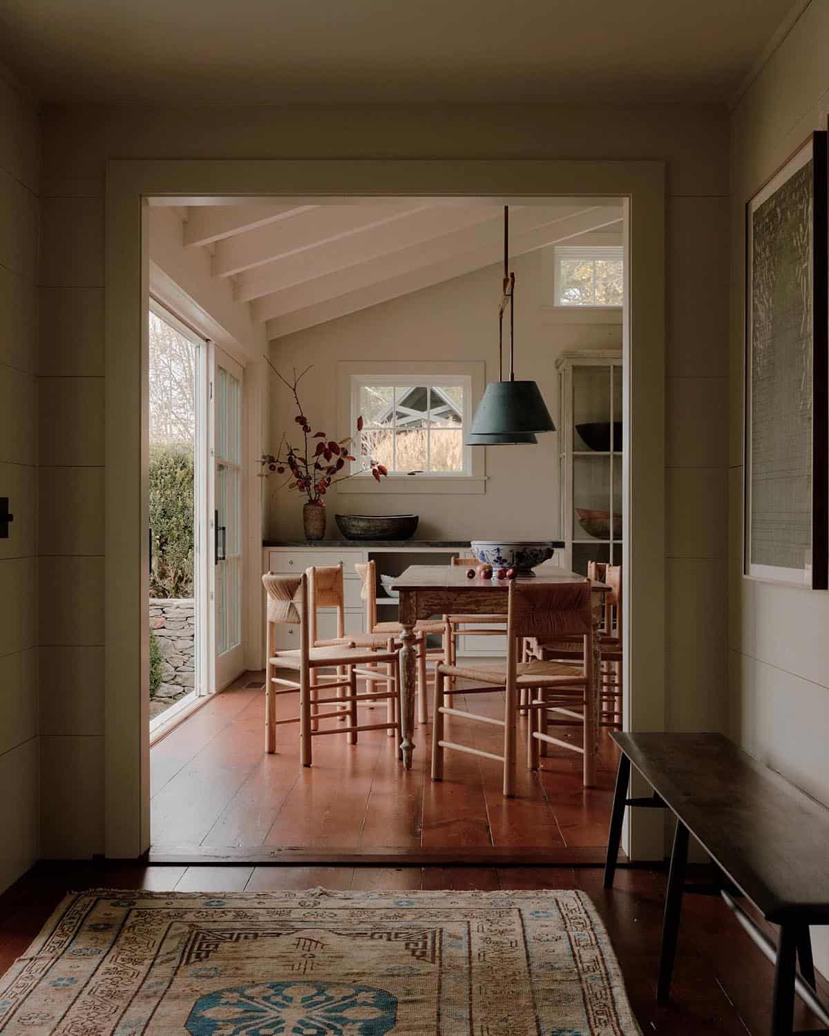View through doorway into dining room with rush-seat chairs, pendant lamp, and sliding glass doors to garden