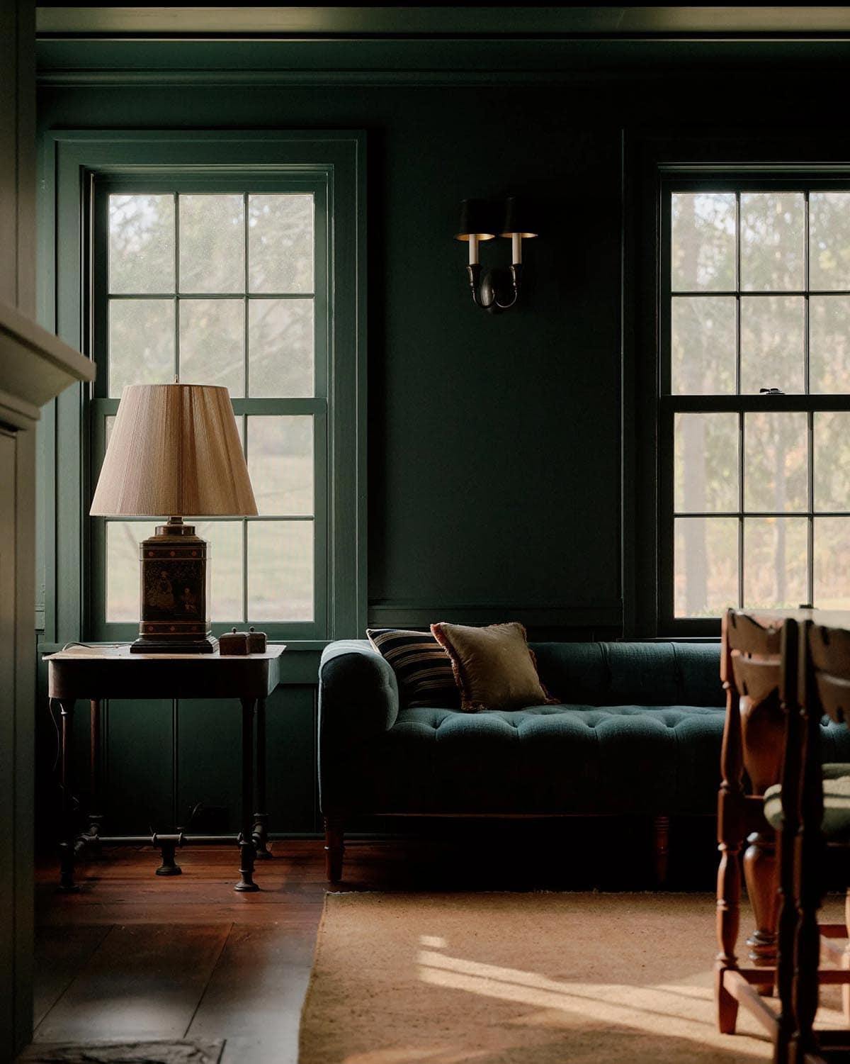 Deep green sitting room with tufted blue-green sofa, antique chinoiserie lamp, and tall gridded windows