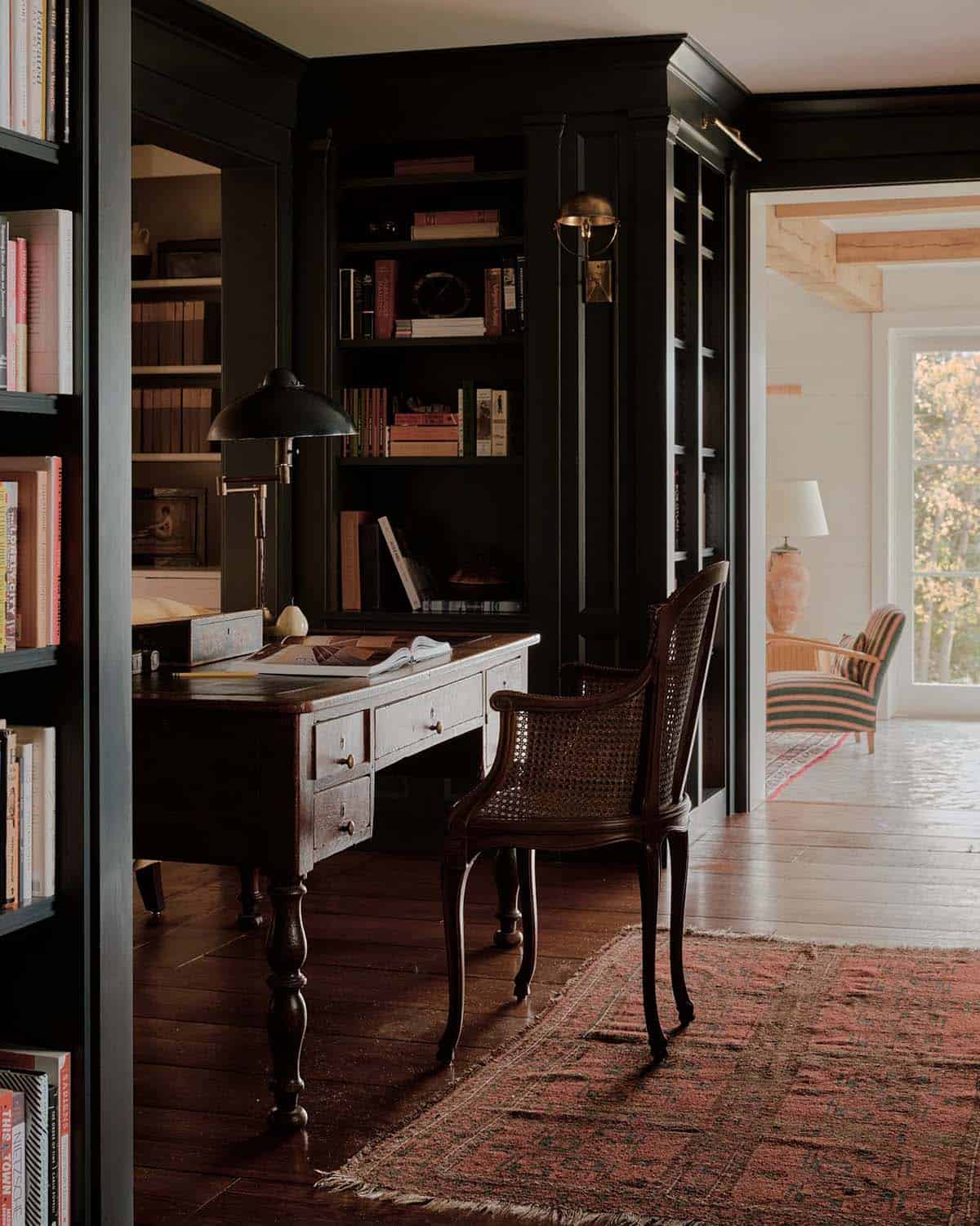Dark-painted home library with antique writing desk, cane chair, and floor-to-ceiling bookshelves