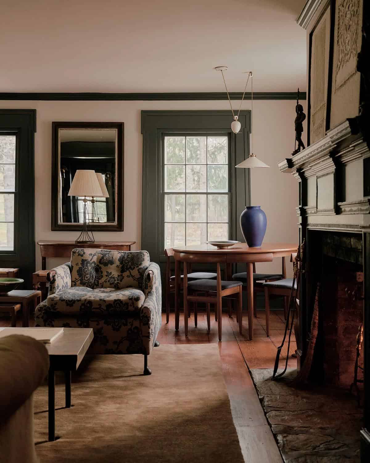 Sitting room with blush walls, dark trim, blue vase on round dining table, floral armchair, and stone fireplace