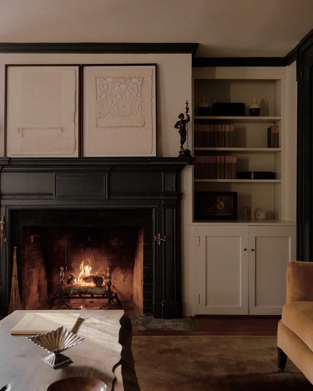 Lit fireplace with dark painted mantel, textile art above, and white built-in shelving beside