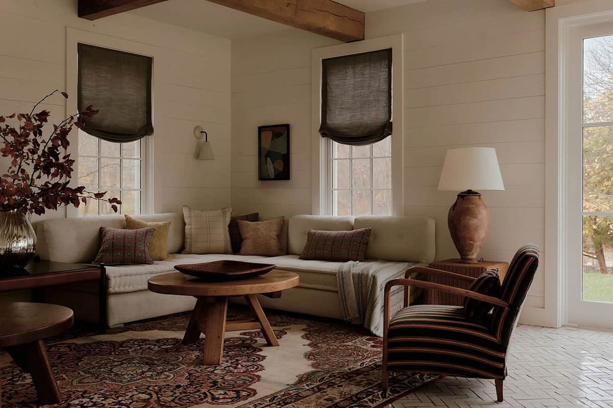 Casual living room with linen sectional, Persian rug, raw wood coffee table, exposed ceiling beams, and linen Roman shades