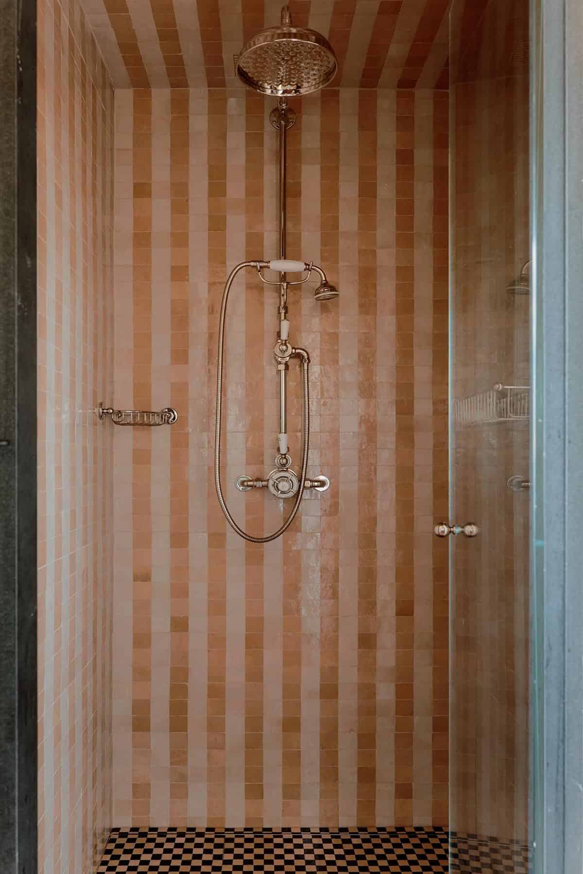 Glass-enclosed shower with terracotta and cream striped zellige tiles and vintage-style chrome fixtures