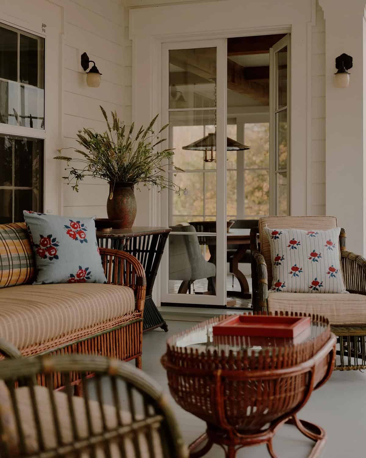Close-up of covered porch with wicker chairs, rose-embroidered pillows, rattan coffee table, and open French doors