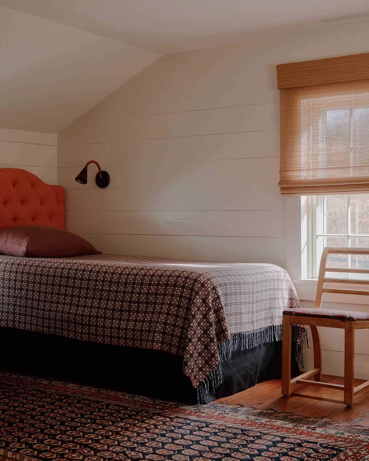 Attic bedroom with terracotta tufted headboard, patterned woven coverlet, woven Roman shade, and Persian rug