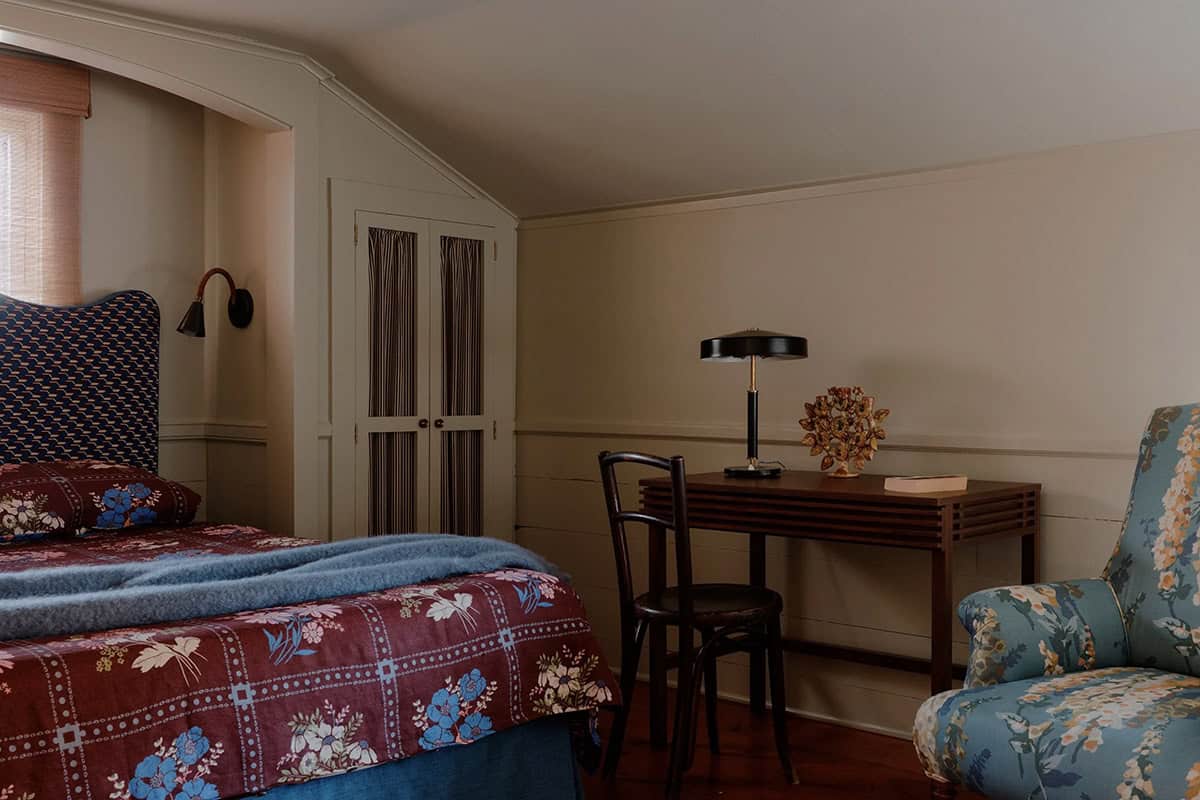 Bedroom with floral print duvet, patterned blue headboard, striped curtain wardrobe doors, and small writing desk