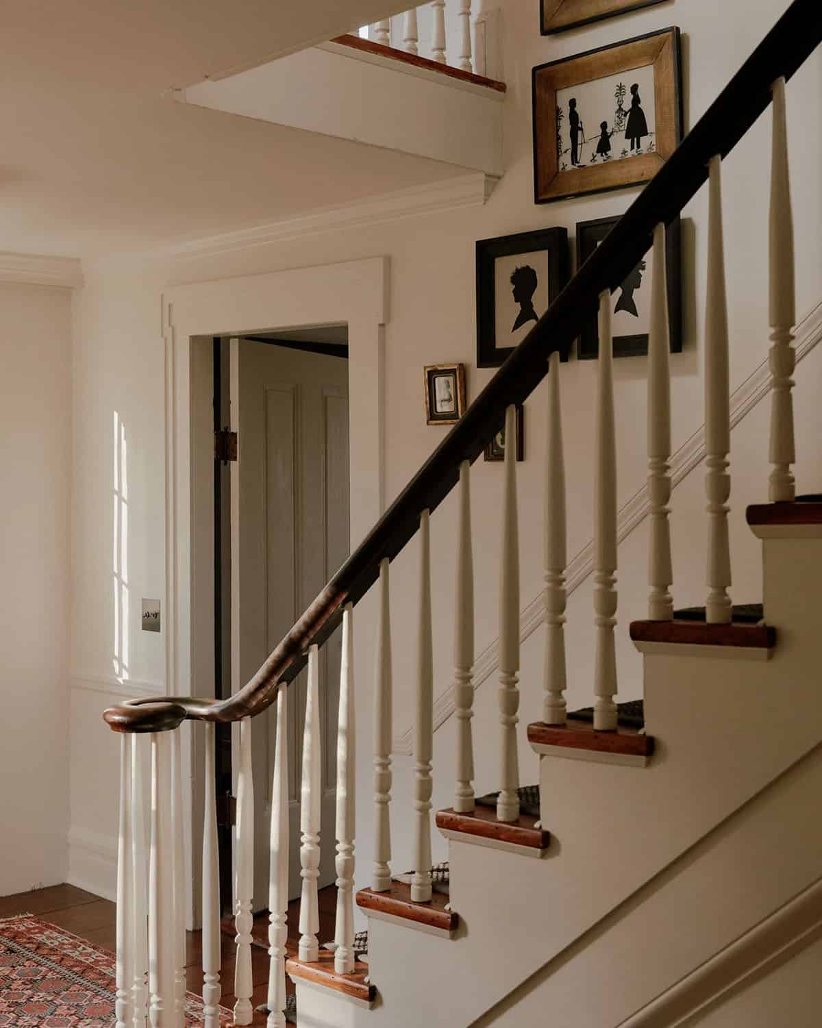 Colonial staircase with turned white balusters, dark wood handrail, and gallery of silhouette portraits along the wall