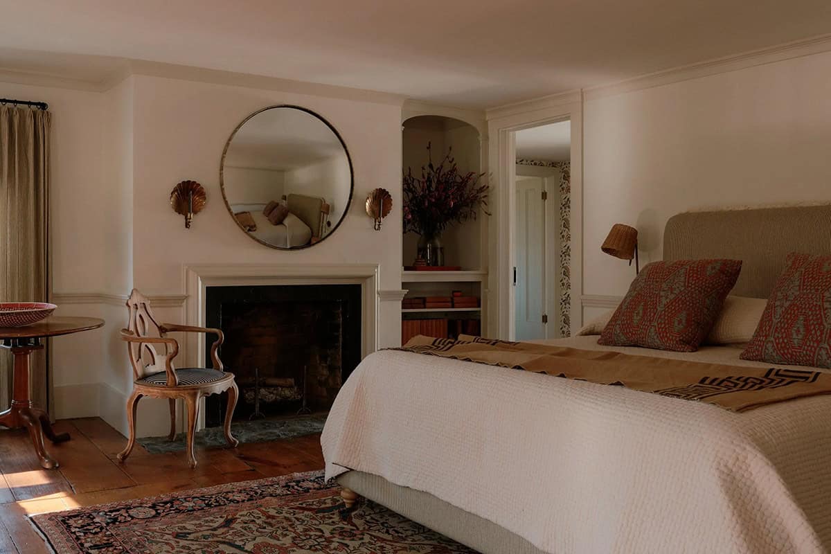 Primary bedroom with fireplace, round brass mirror, shell sconces, Persian rug, upholstered headboard, and arched alcove