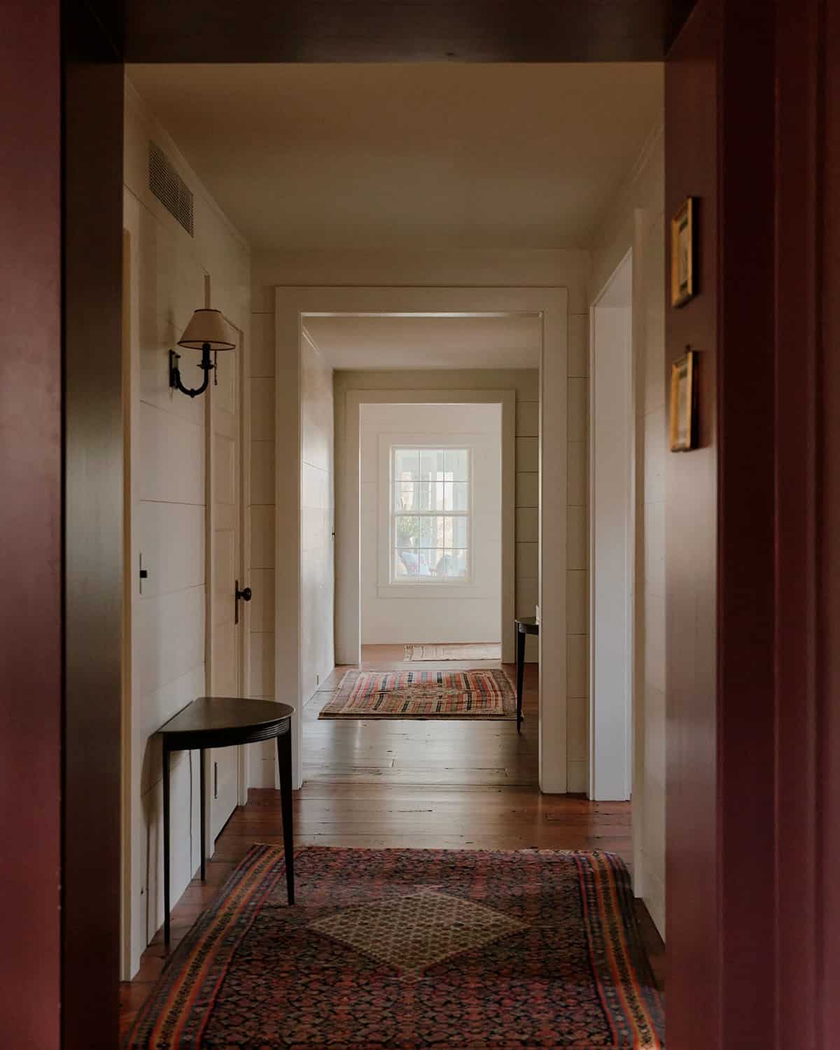 Long farmhouse hallway with shiplap walls, layered Persian runners, demilune table, and enfilade of doorways