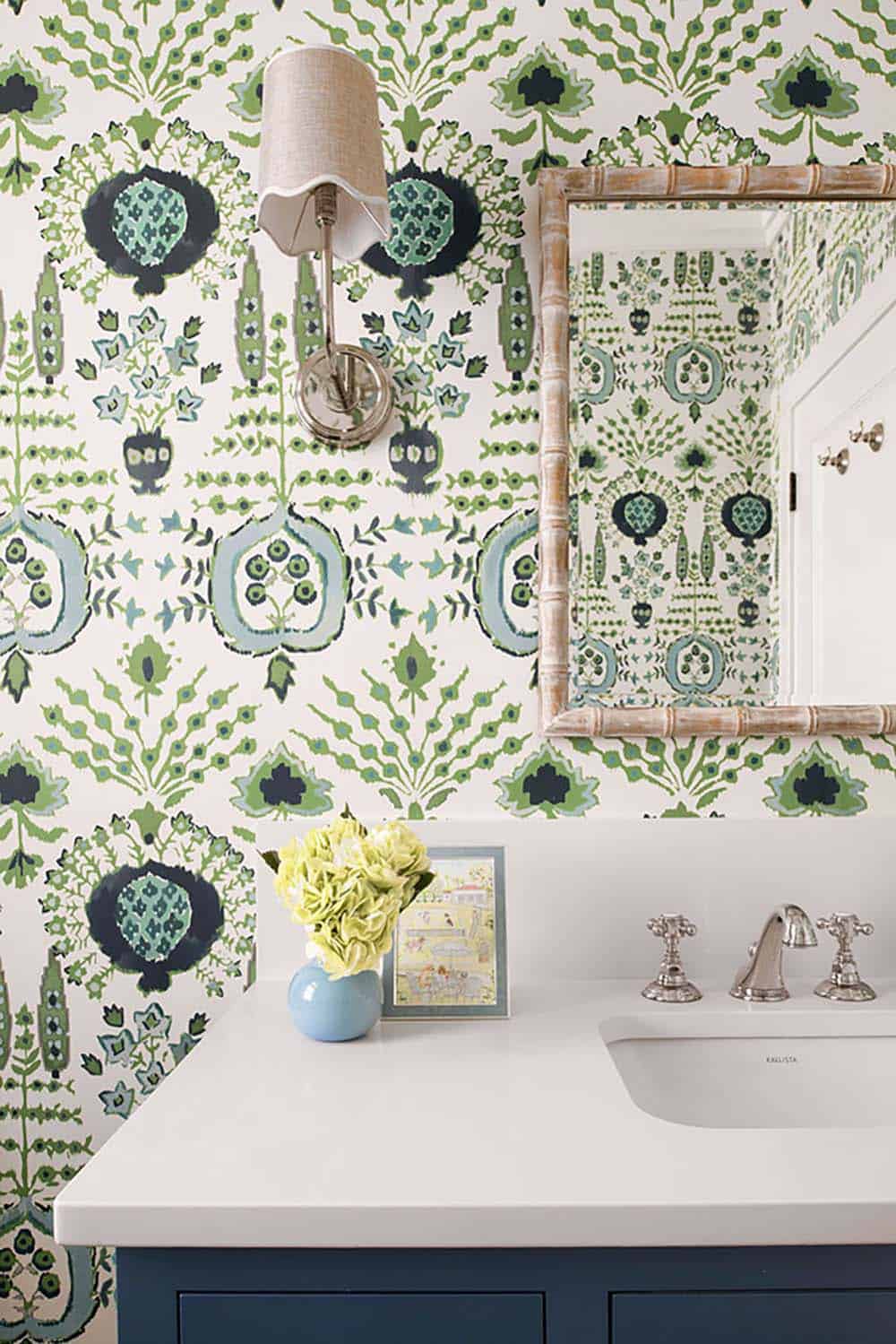 Powder room with bold green botanical wallpaper, bamboo mirror, and navy vanity
