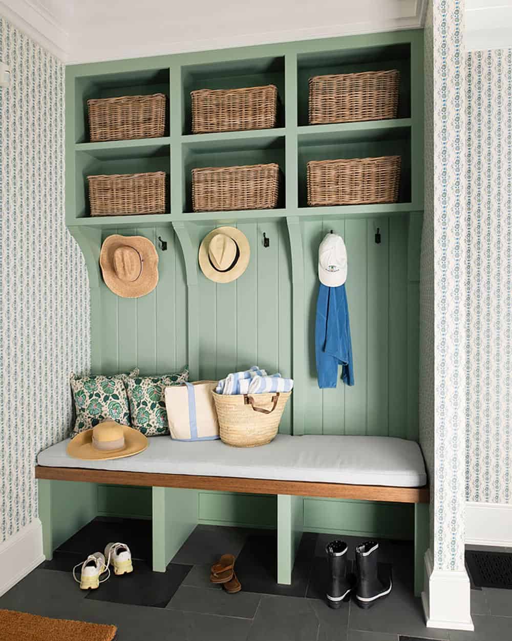 Sage green mudroom built-ins with wicker baskets, coat hooks, and upholstered bench