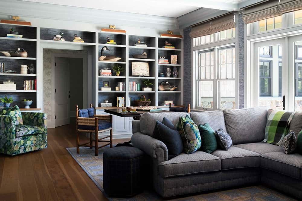 Family room with gray sectional, grasscloth built-in bookshelves, and stone fireplace