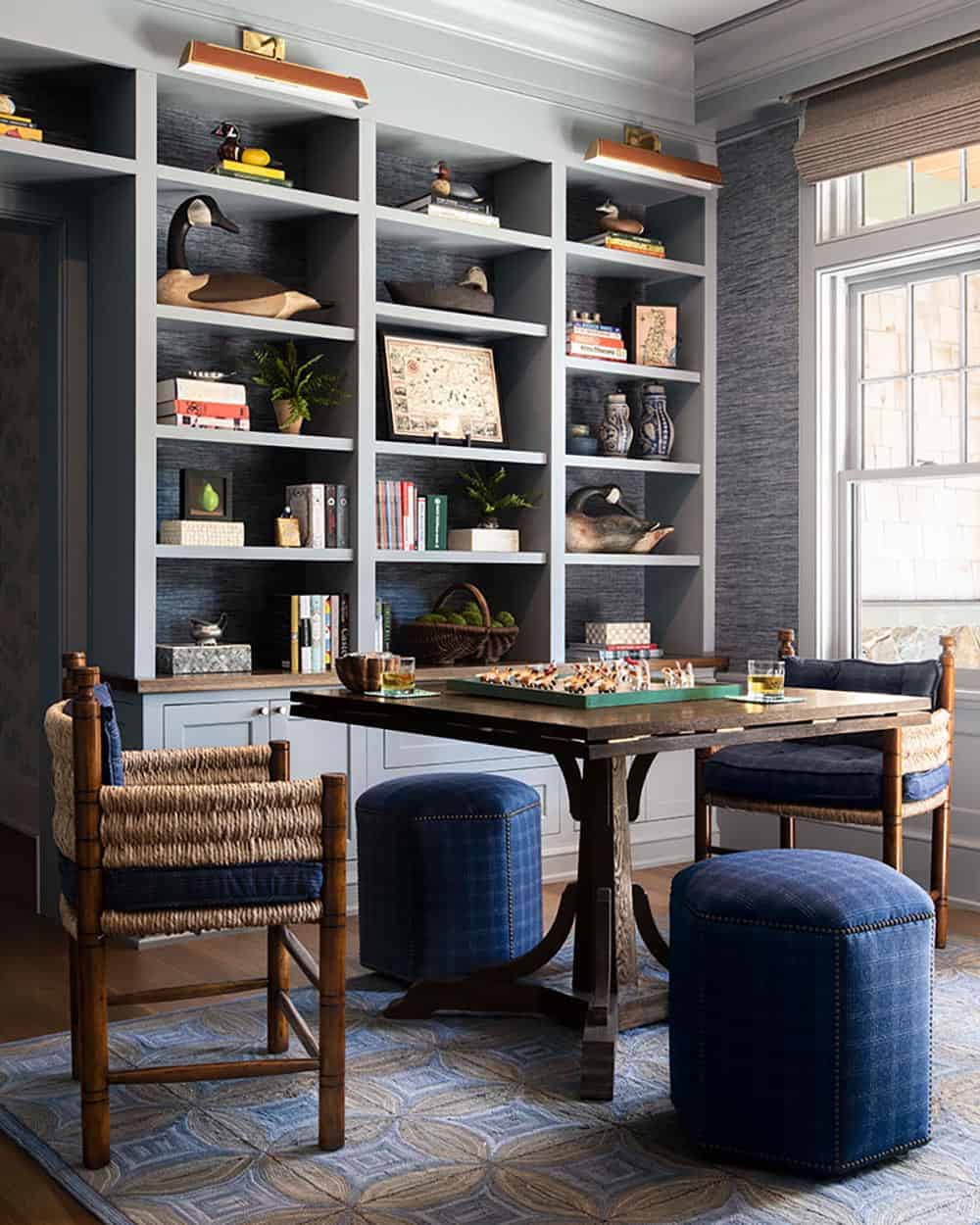 Game room with navy grasscloth built-ins, games table, rattan chairs, and blue ottomans