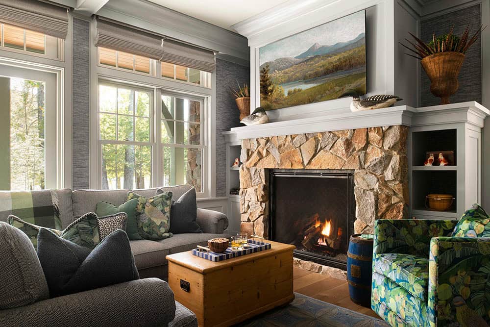 Living room with stone fireplace, gray sofas, botanical accent chair, and landscape painting