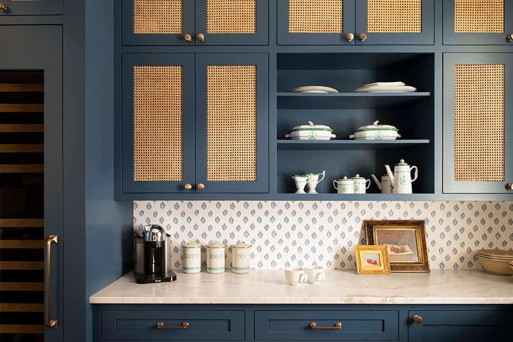 Navy butler's pantry with cane-front cabinet doors, brass hardware, and patterned tile backsplash