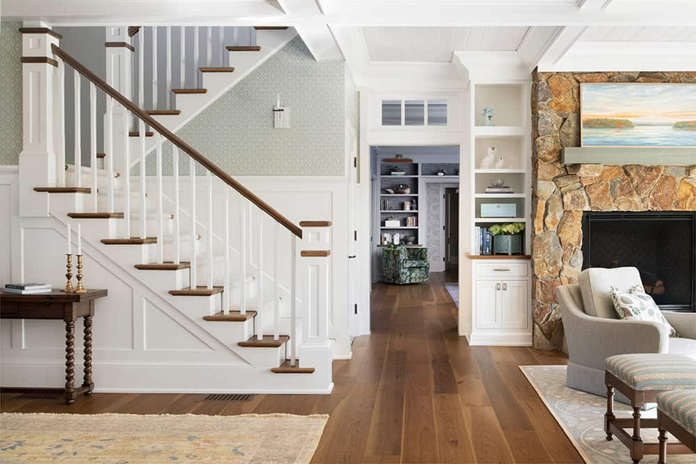 Entry hall with white staircase, wood treads, patterned wallpaper, and stone fireplace