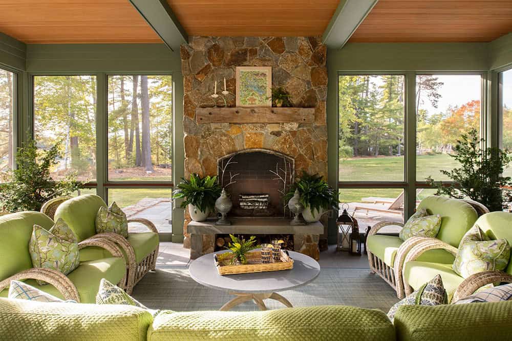 Screened porch with floor-to-ceiling stone fireplace, cedar ceiling, and green wicker furniture