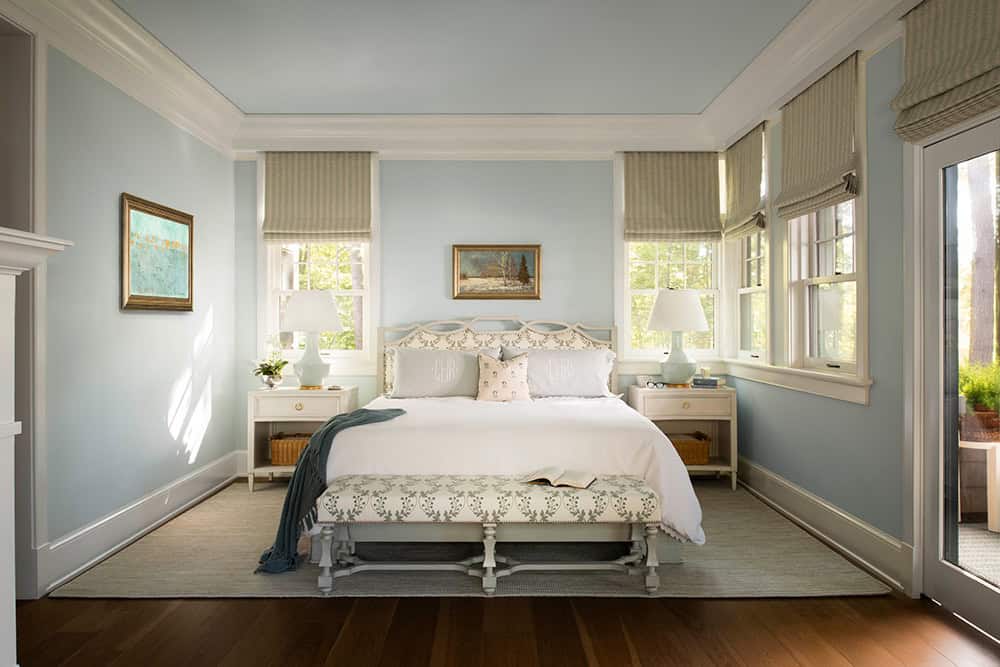 Primary bedroom with powder blue walls, upholstered headboard, and striped Roman shades