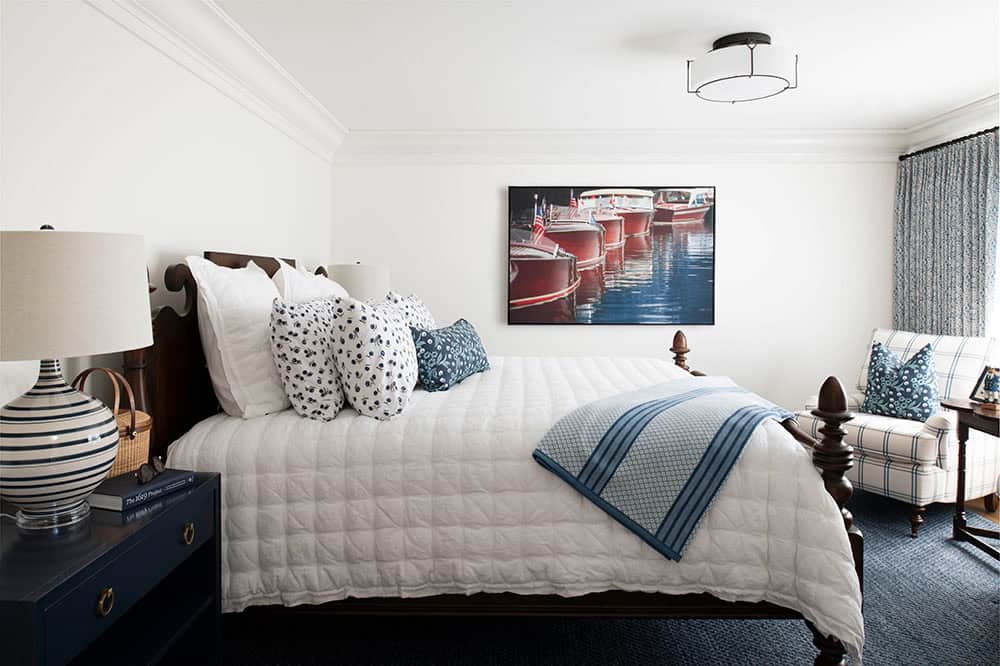 Guest bedroom with dark wood four-poster bed, navy carpet, and classic boat photography