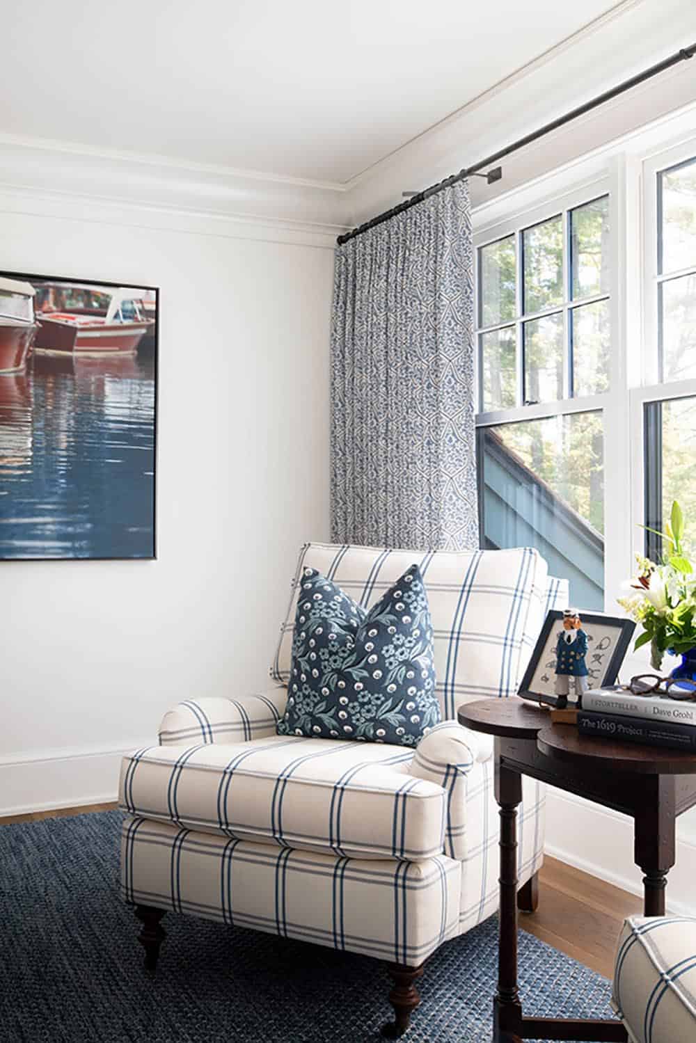 Blue plaid reading chair with patterned drapes and vintage boat artwork in guest bedroom