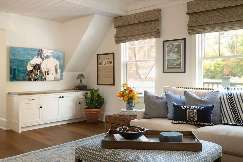 Upper-level sitting room with vaulted ceiling, blue upholstered ottoman, and Wolfeboro memorabilia