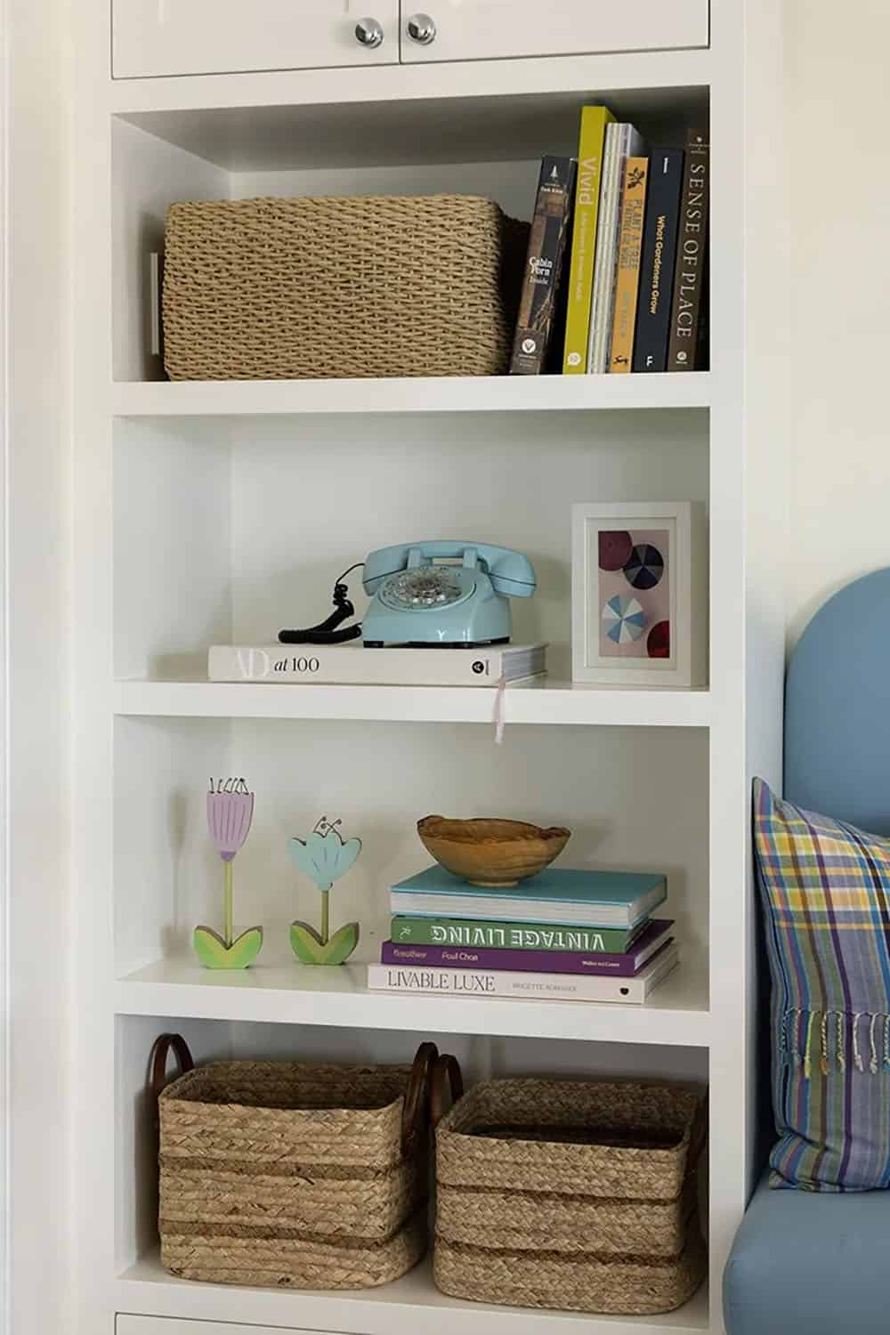 White built-in bookshelf styled with wicker baskets, vintage blue rotary phone, small framed art, and decorative books