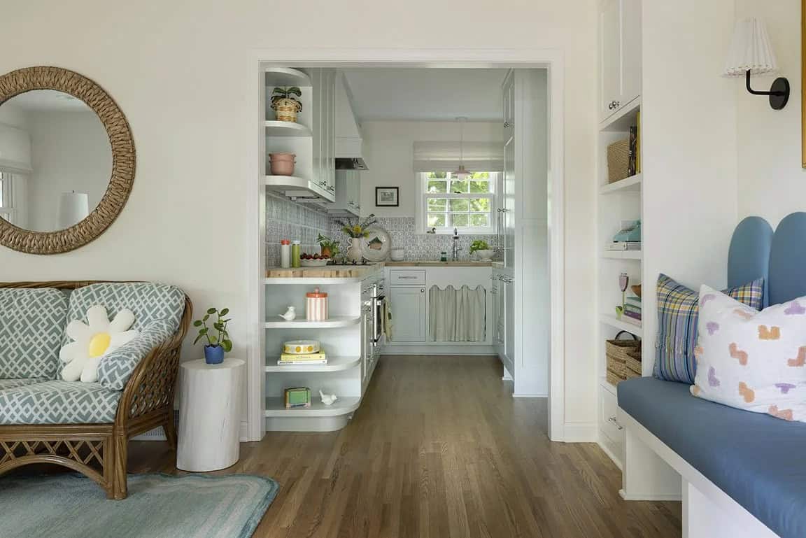 Open-plan view from living room into sage green kitchen with curved corner shelves and rattan sofa with daisy pillow
