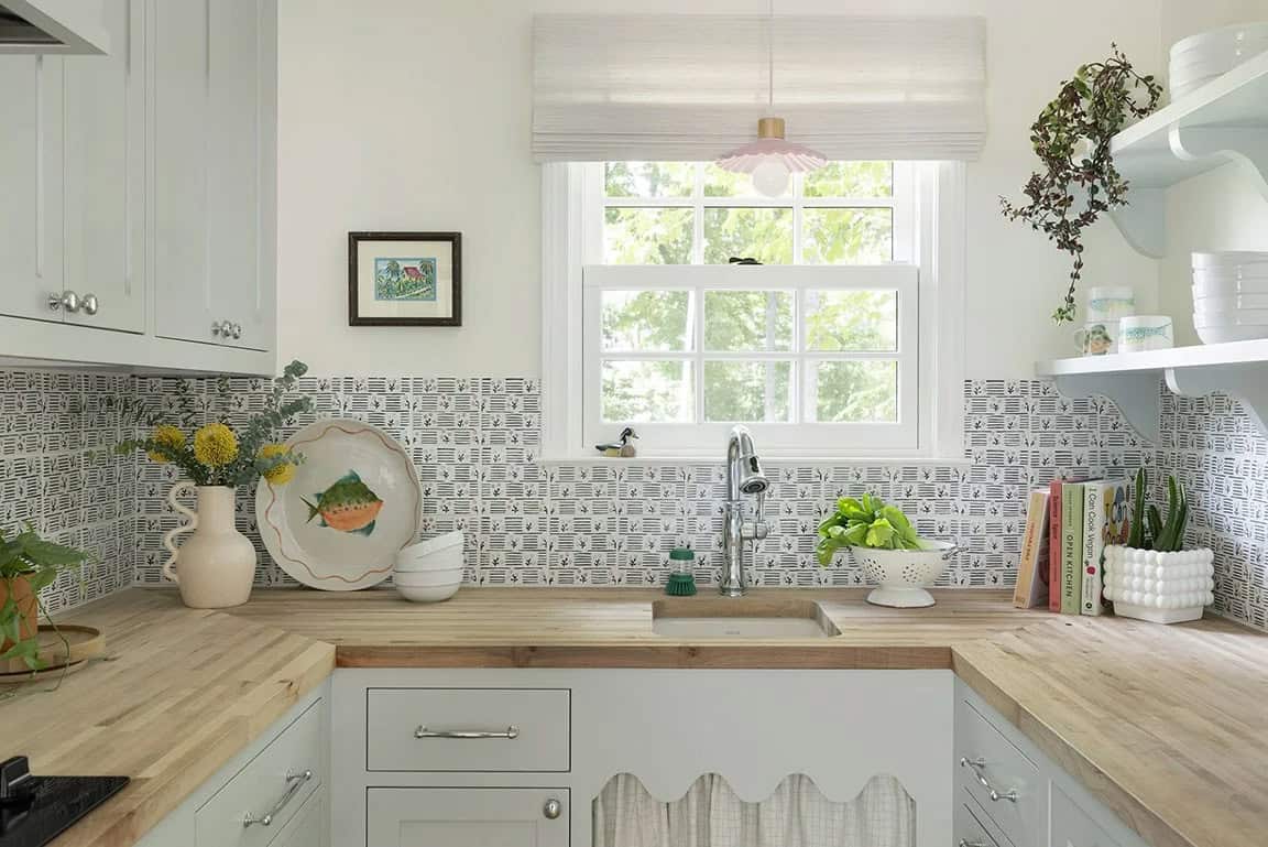 Compact kitchen with sage green cabinets, butcher block counters, patterned tile backsplash, and pink scalloped pendant light