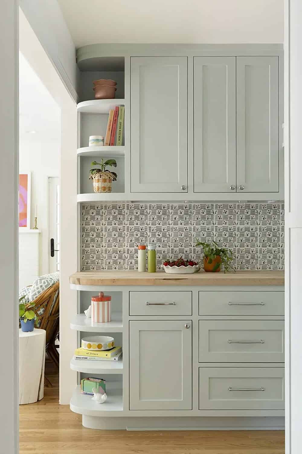 Sage green kitchen cabinetry with curved open corner shelving, patterned backsplash tile, and butcher block countertop