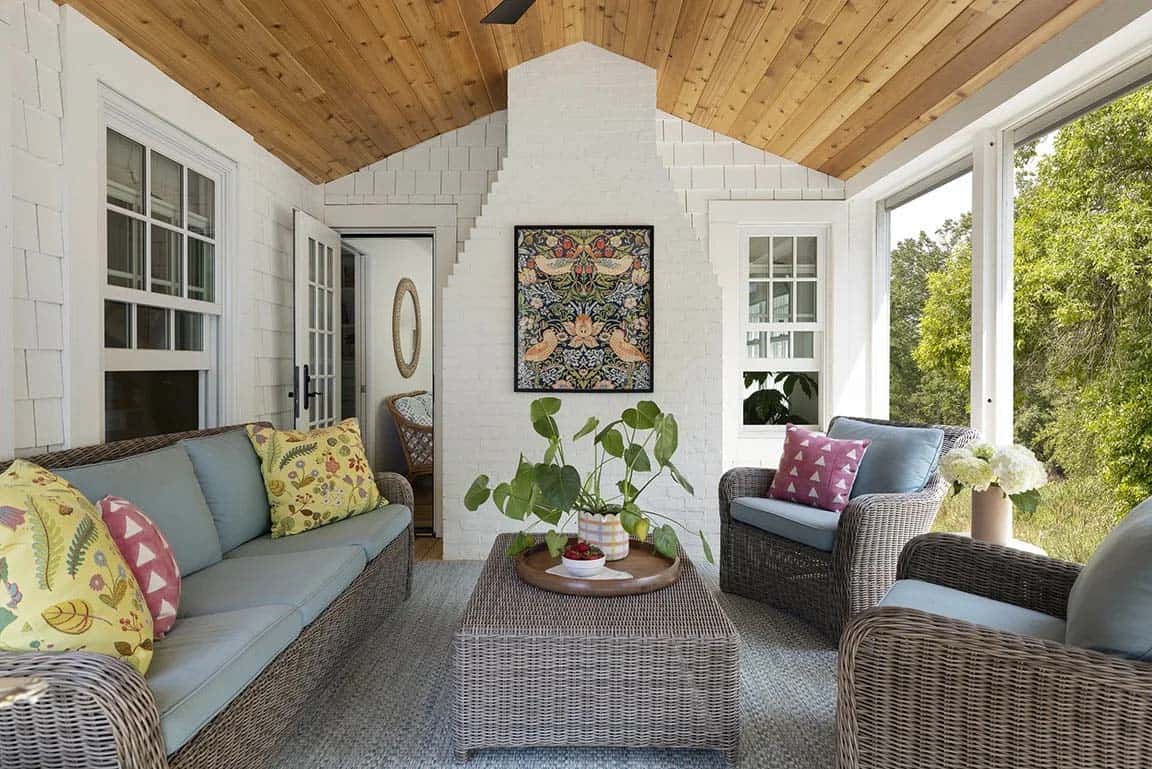 Screened porch with wicker furniture, blue cushions, cedar ceiling, white painted brick, and William Morris artwork