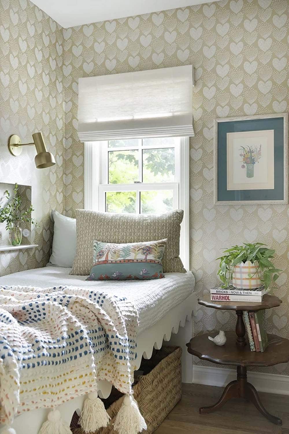 Cozy bedroom nook with heart-pattern wallpaper, scallop-trimmed daybed, tassel throw, and vintage side table