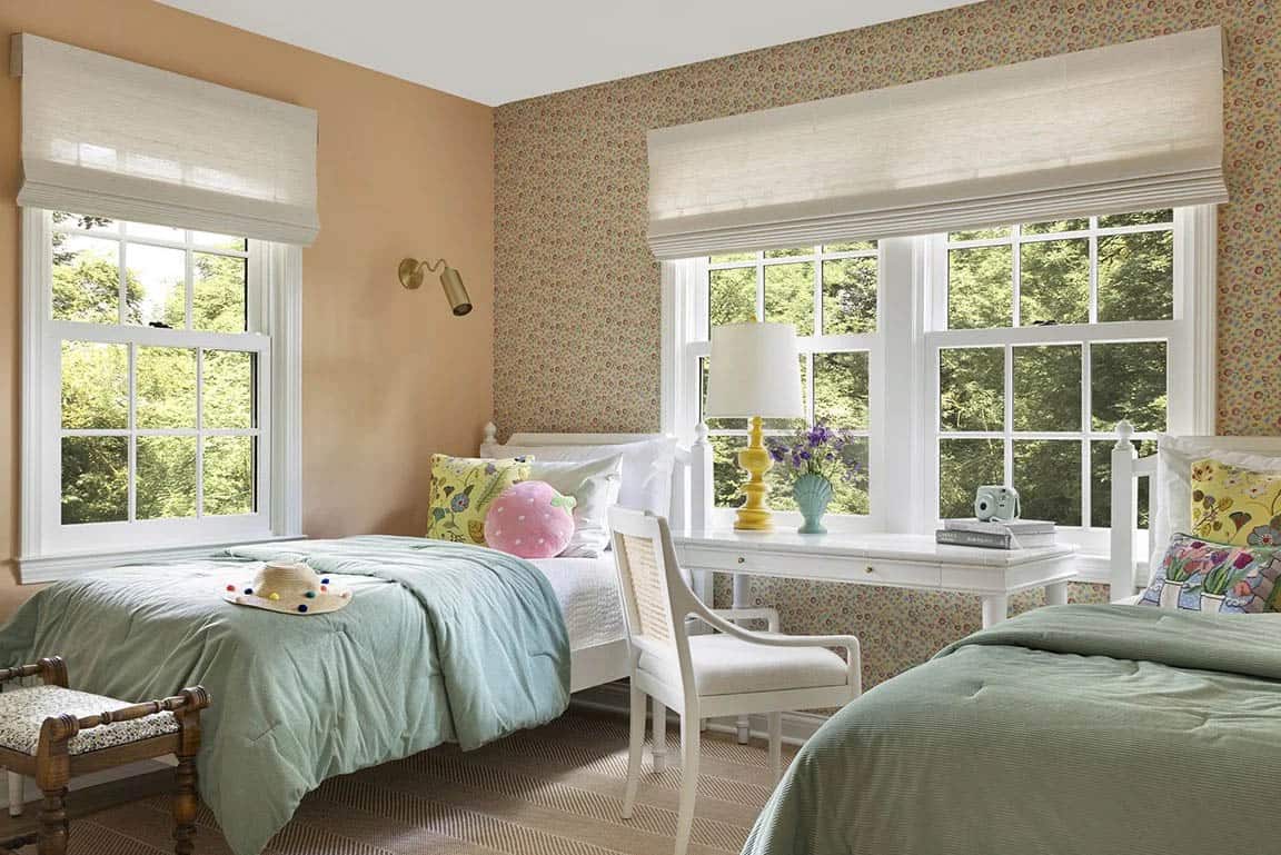 Children's bedroom with twin beds, peach walls, floral wallpaper border, sage green bedding, and white desk