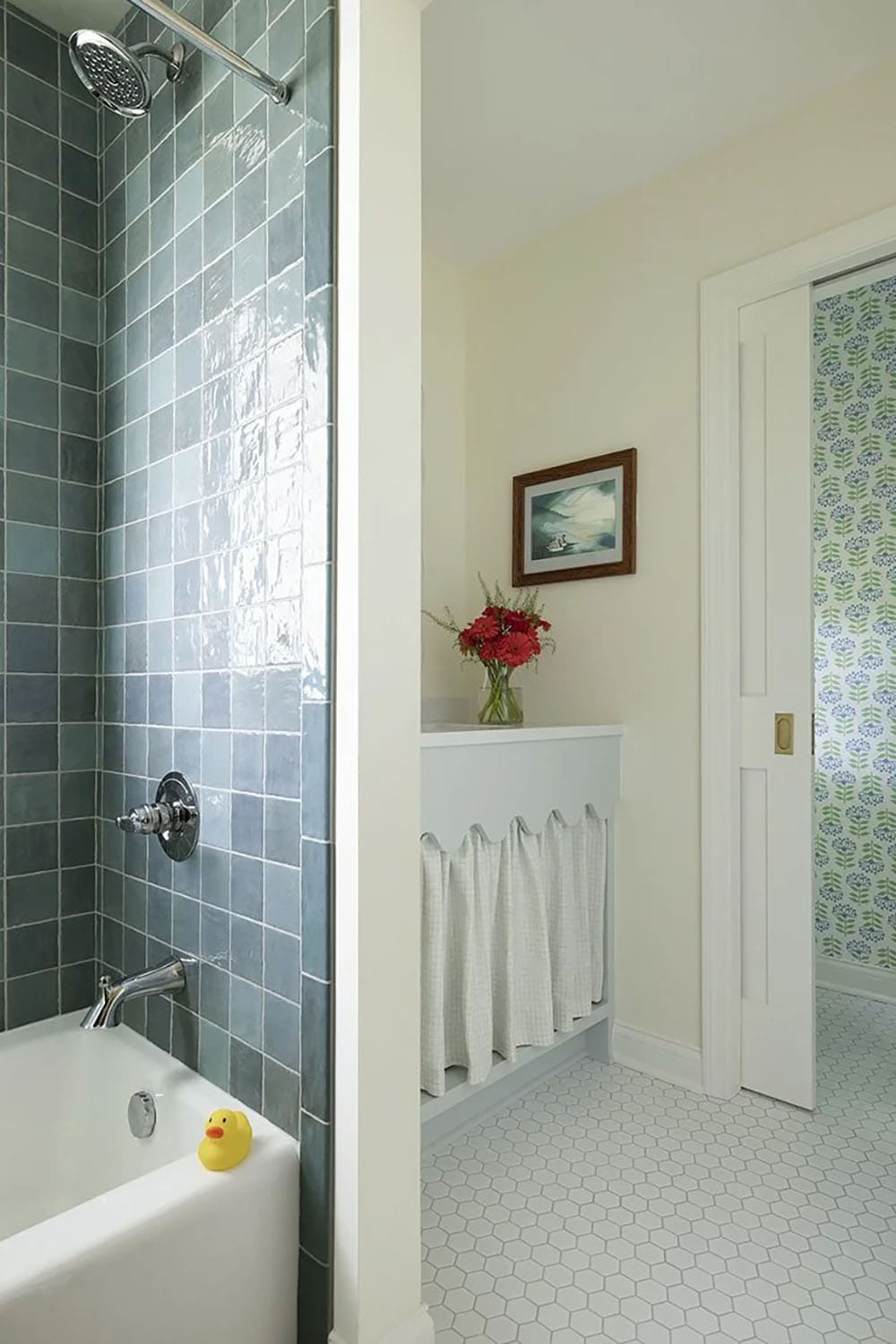 Bathroom detail showing teal tile tub surround, yellow rubber duck, and doorway with green floral wallpaper beyond