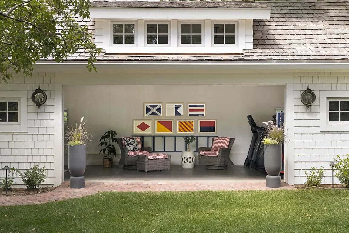 Cape Cod style garage exterior with cedar shingle siding, framed nautical flag prints, and wicker chairs with striped cushions