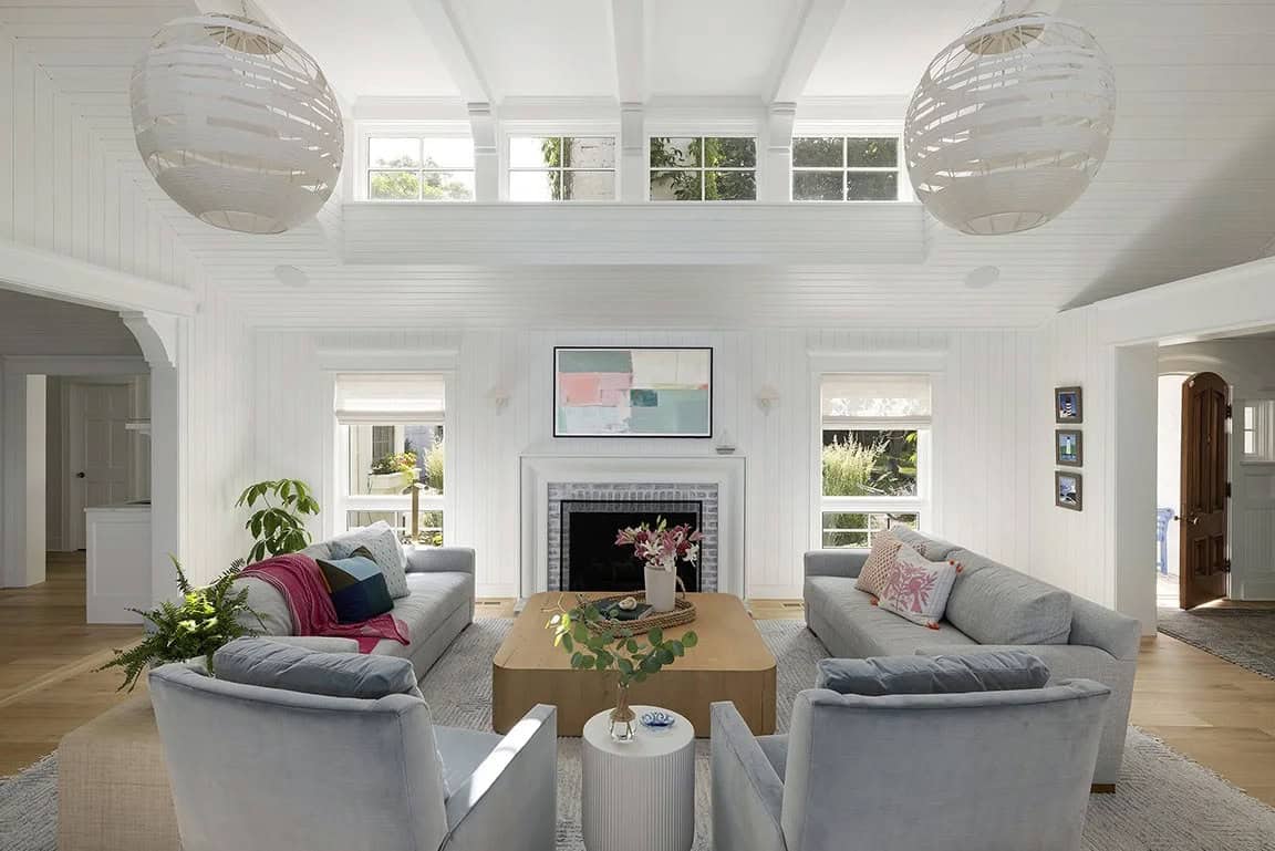Bright living room with double globe pendants, clerestory windows, symmetrical gray sofas, brick fireplace, and abstract art