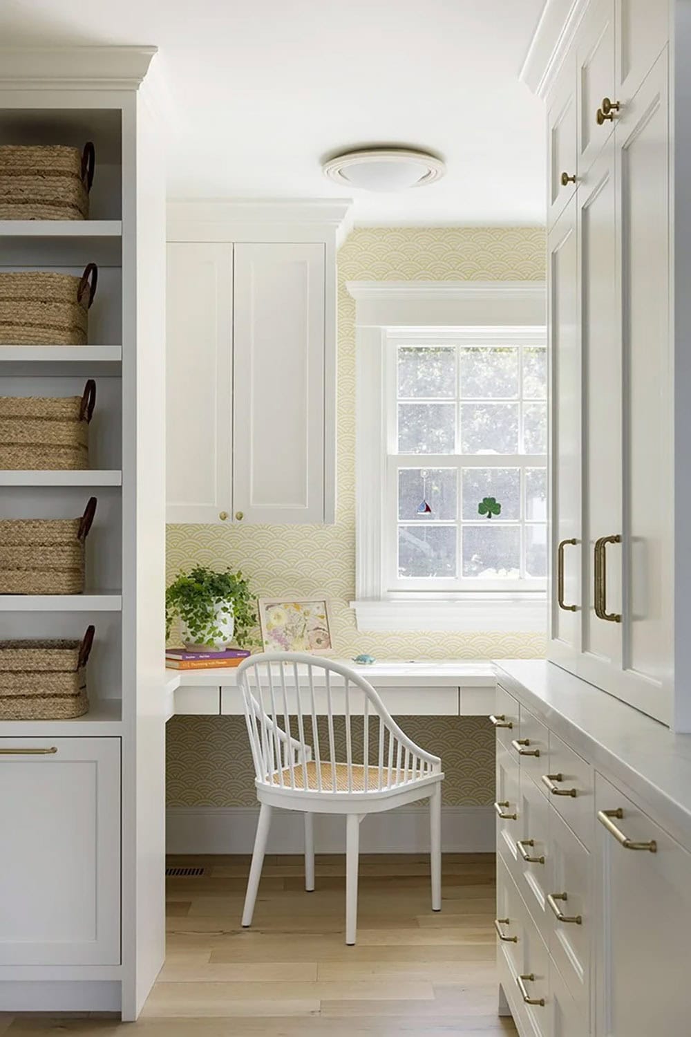 Mudroom desk nook with yellow scallop wallpaper, built-in white desk, Windsor chair, and floor-to-ceiling wicker basket shelving