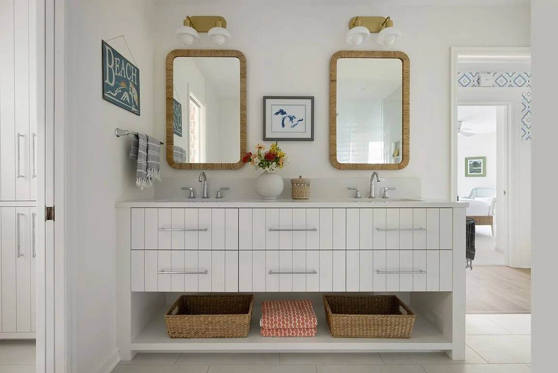 Double vanity with rattan-framed mirrors, gold sconces, shiplap drawer fronts, wicker baskets below, and Great Lakes map art