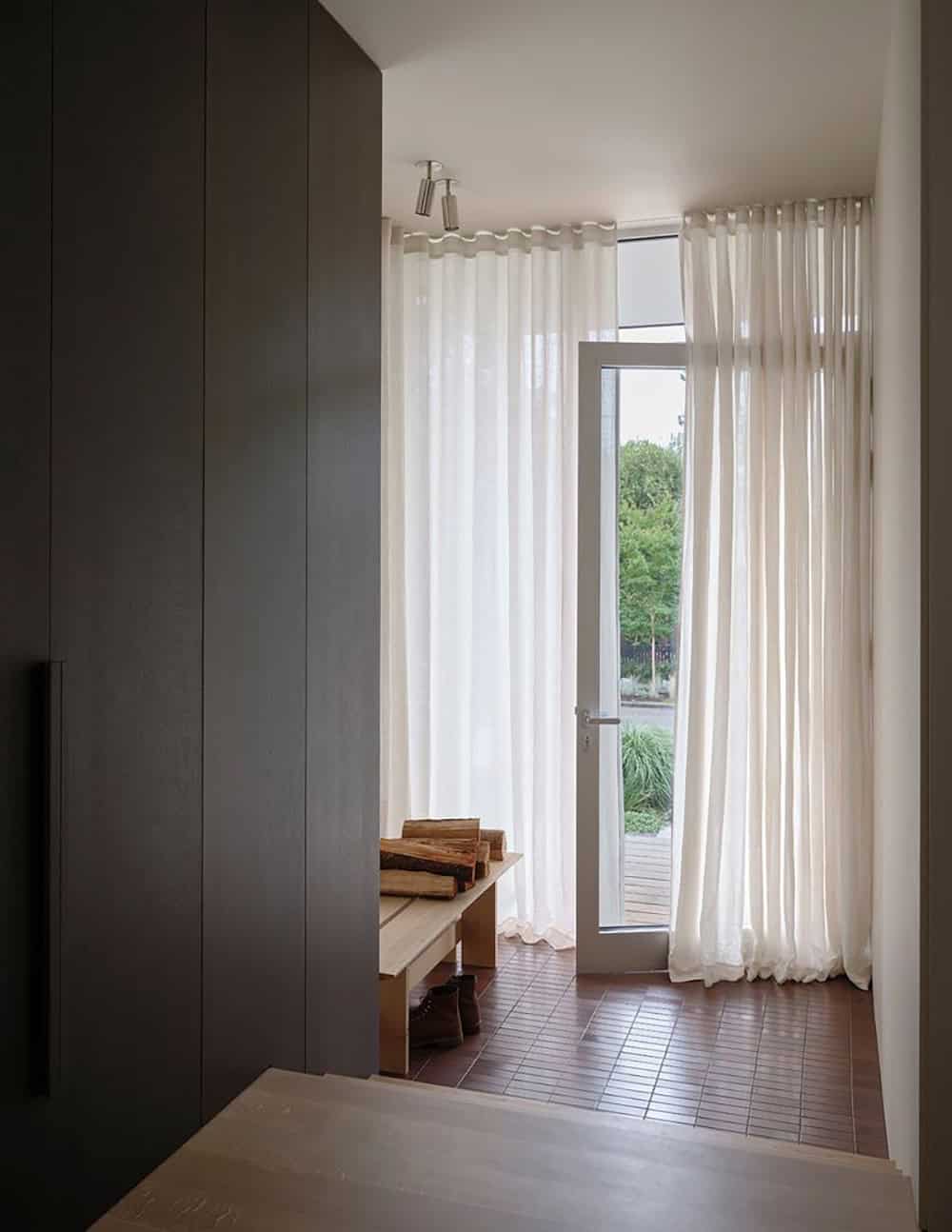 Mudroom entry with dark cabinetry, wood bench, and sheer curtains leading to the back garden