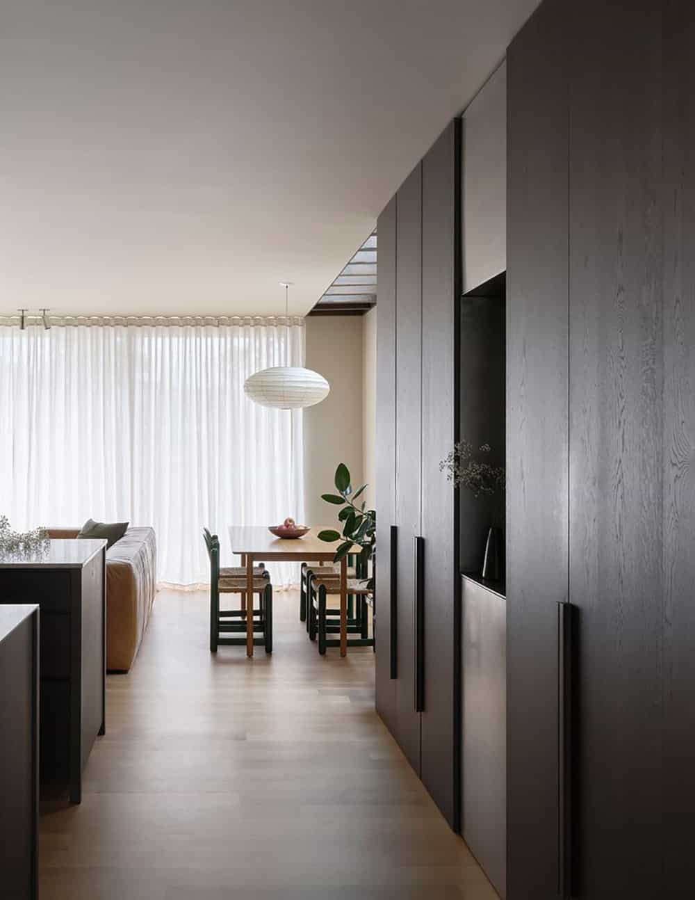 Open living and dining area with dark cabinetry wall, paper pendant light, and perimeter skylight