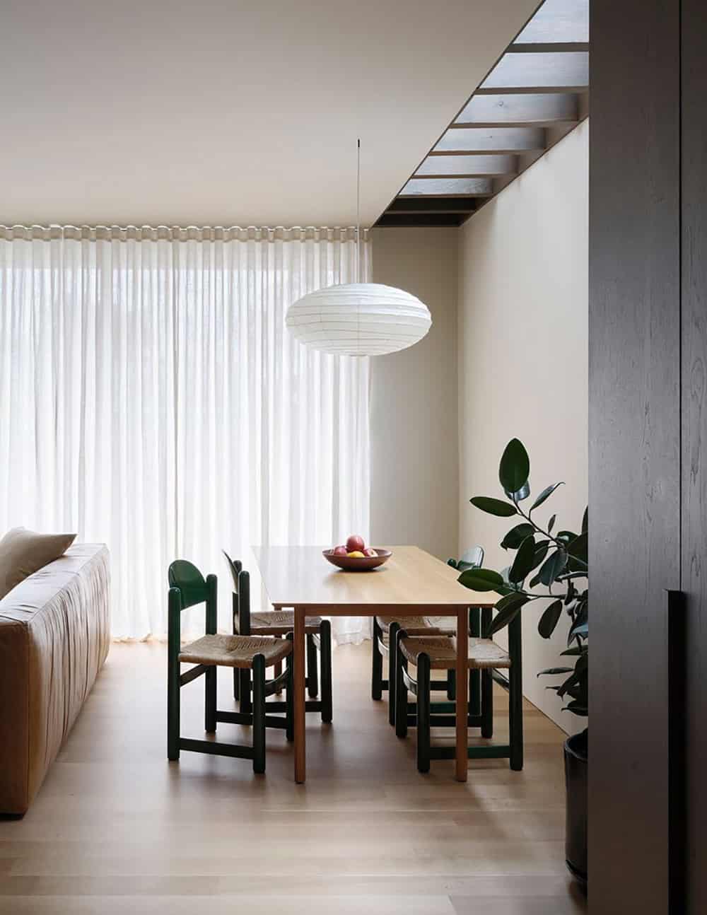 Dining area with green rush-seat chairs, wood table, and open stair above
