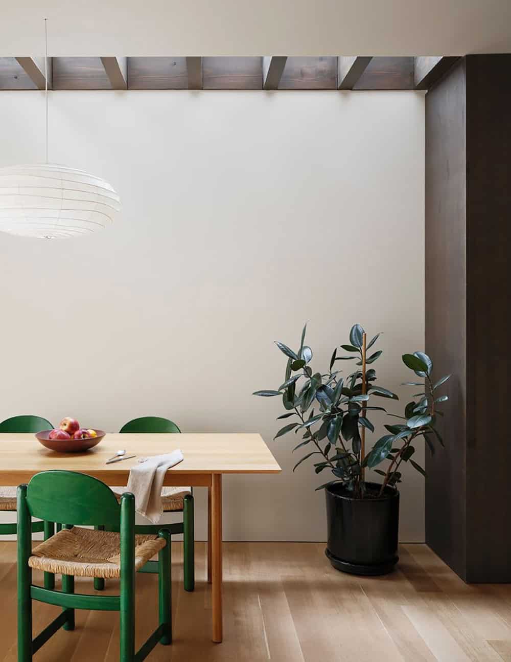 Dining nook with green chairs, wood table, exposed dark beams, and a rubber plant