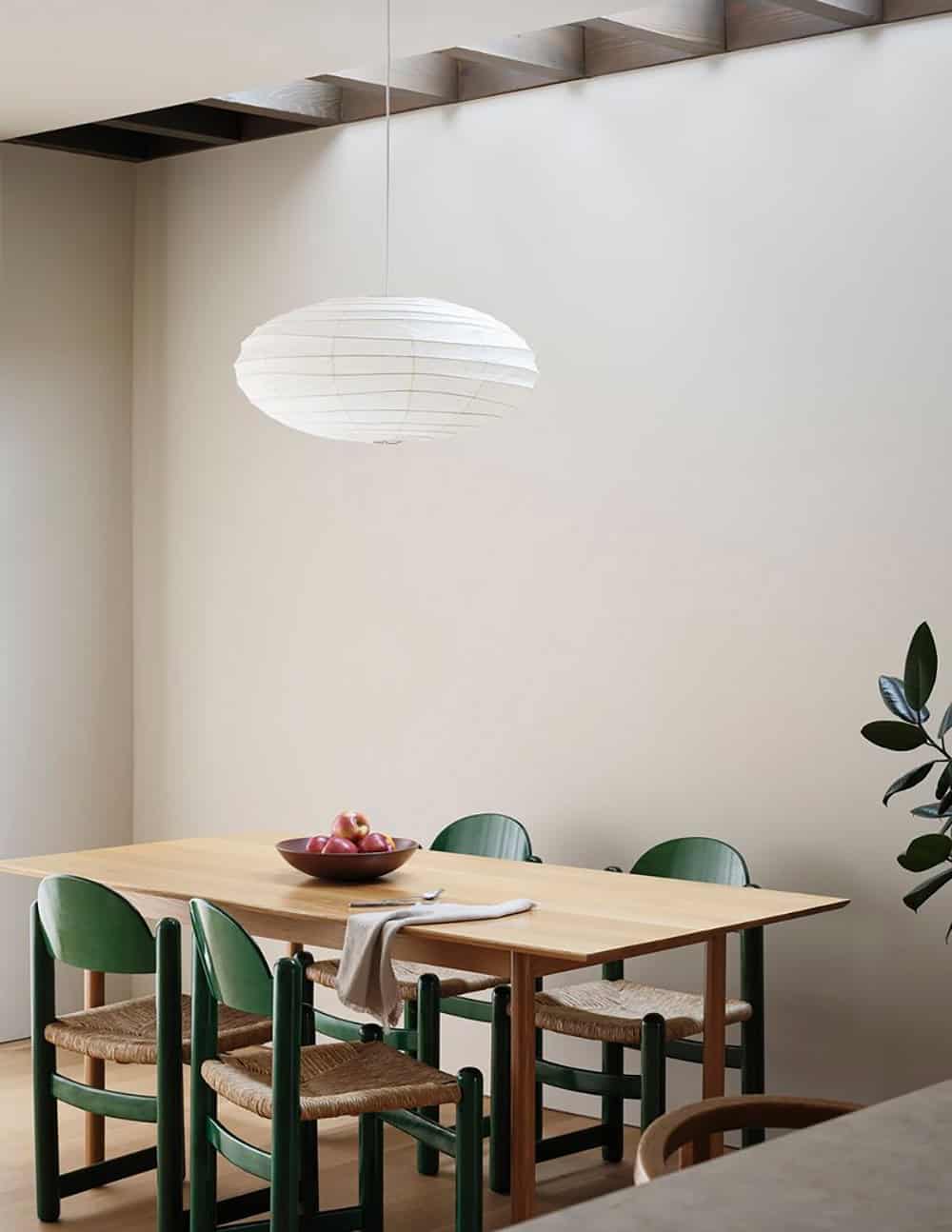 Dining table with green chairs beneath a paper pendant light and exposed ceiling beams