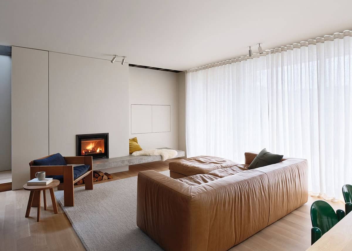 Light-filled living room with leather sofa, fireplace, and floor-to-ceiling sheer curtains