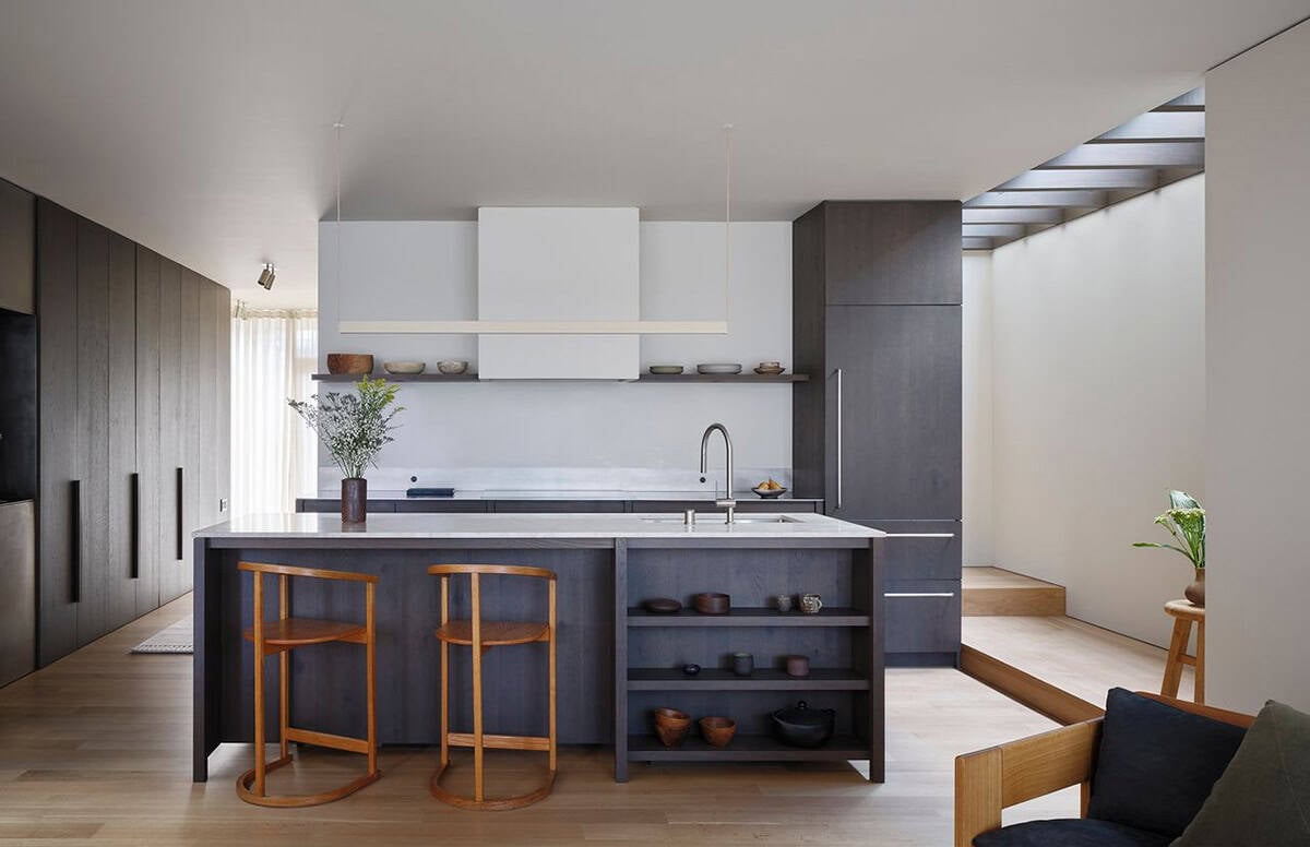 Kitchen with dark wood island, open shelving, white range hood, and perimeter skylight