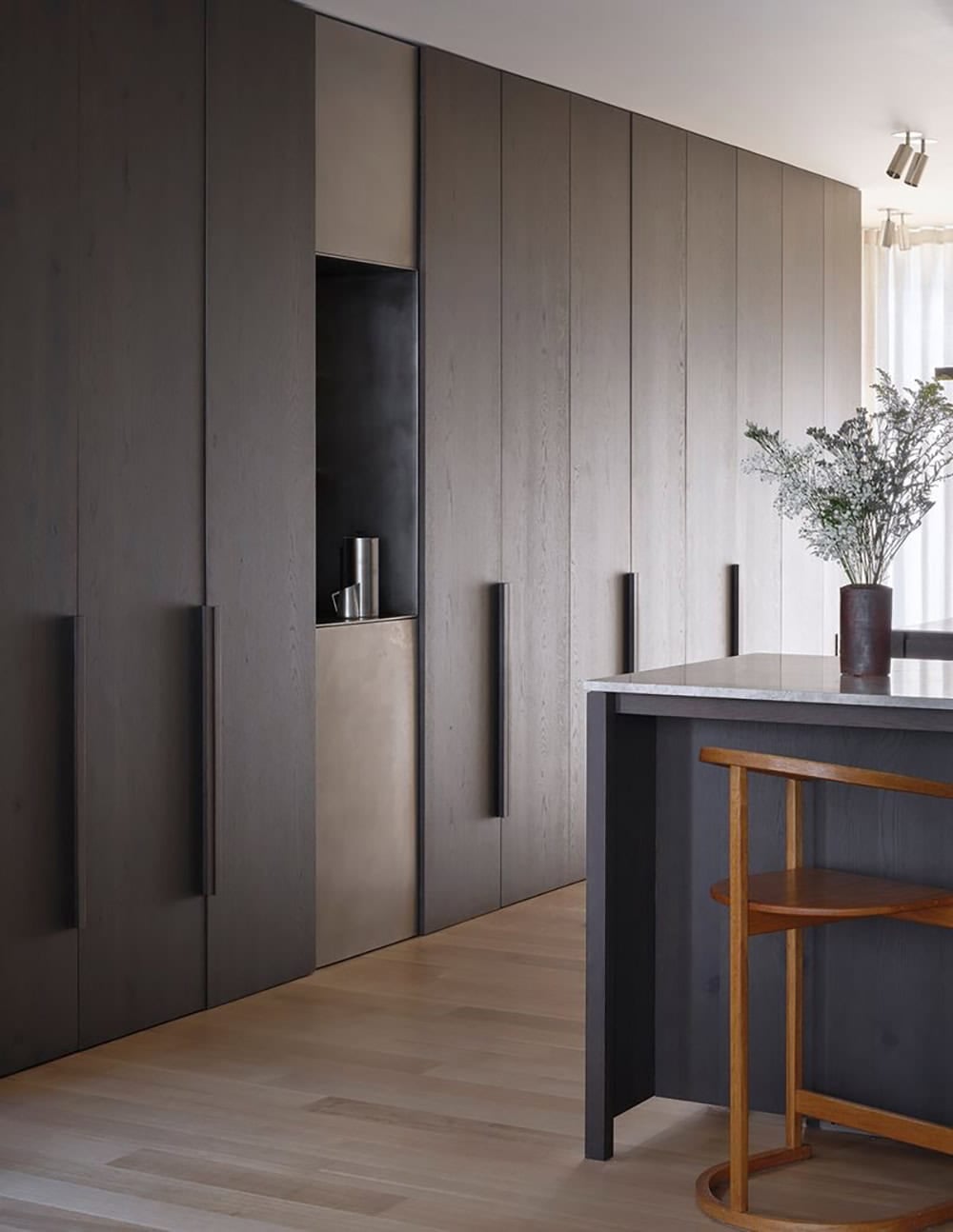 Dark stained oak cabinetry wall with brushed metal niche and kitchen island detail