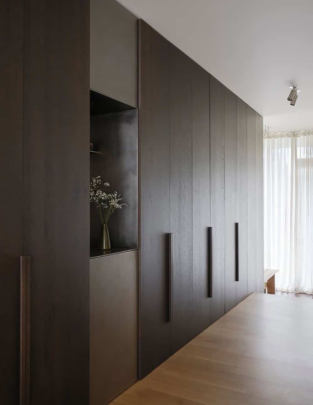 Full-height dark cabinetry wall with metal niche and sheer curtain at corridor end