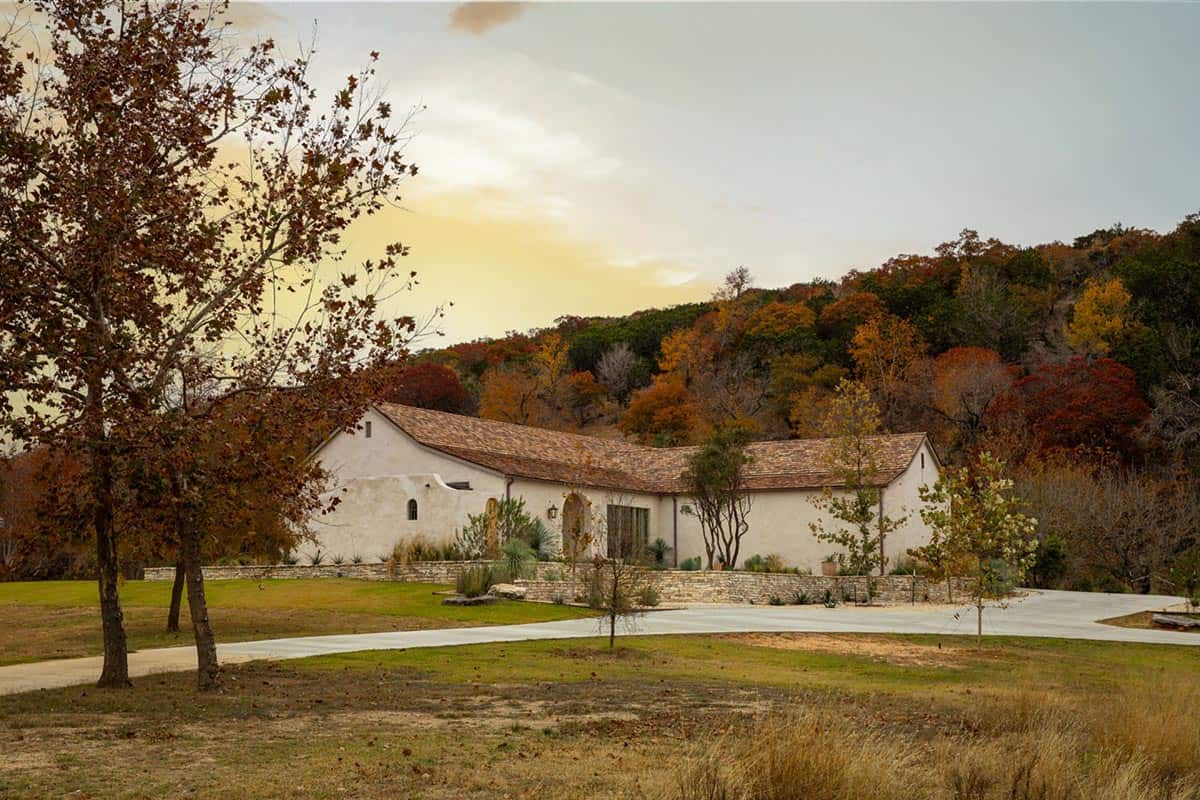 White stucco hacienda with cedar shake roof nestled among fall foliage in Texas Hill Country