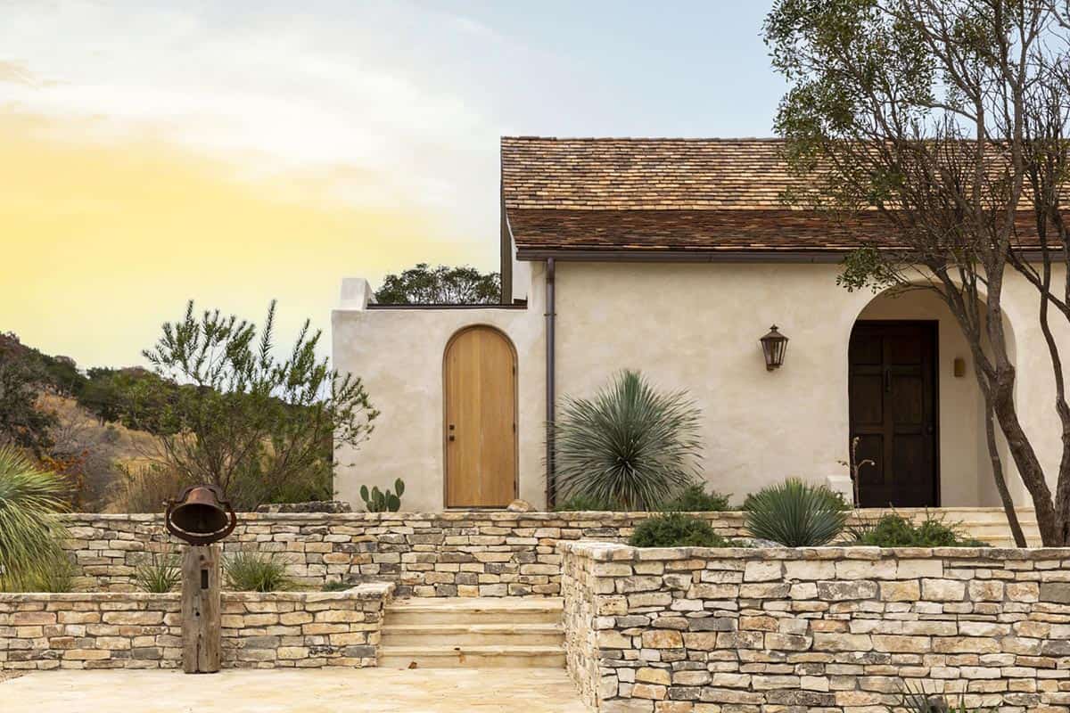 Mediterranean-style home exterior with arched wooden door, limestone steps, and desert plantings
