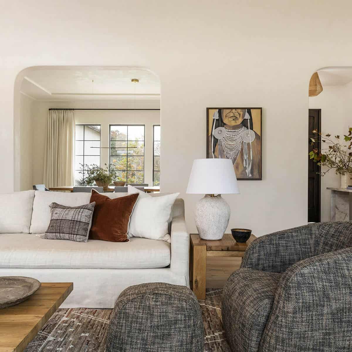 Living room with cream linen sofa, rust velvet pillows, ceramic lamp, and portrait painting